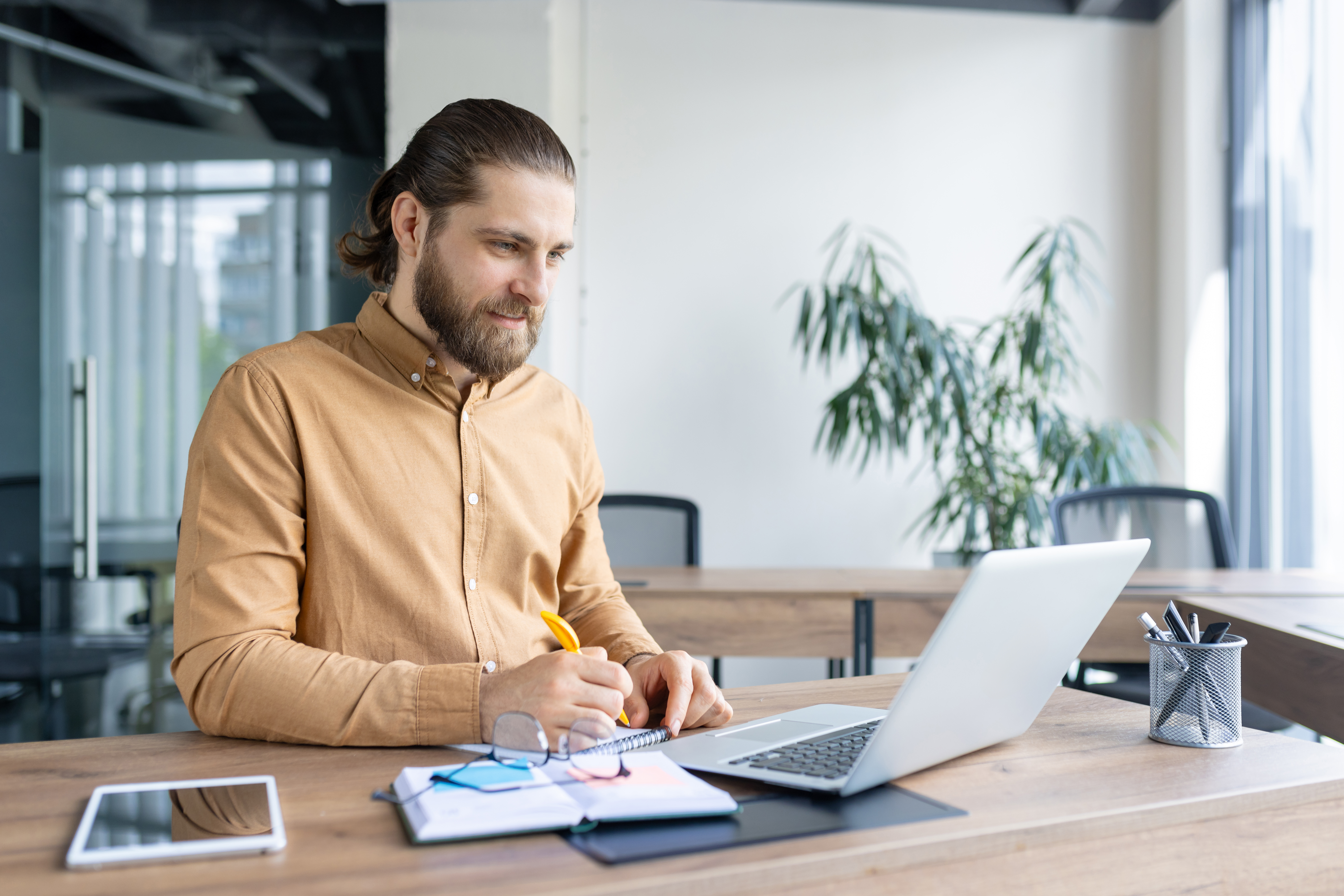 Mann sitzt in leerem Büro vor Laptop und macht sich Notizen