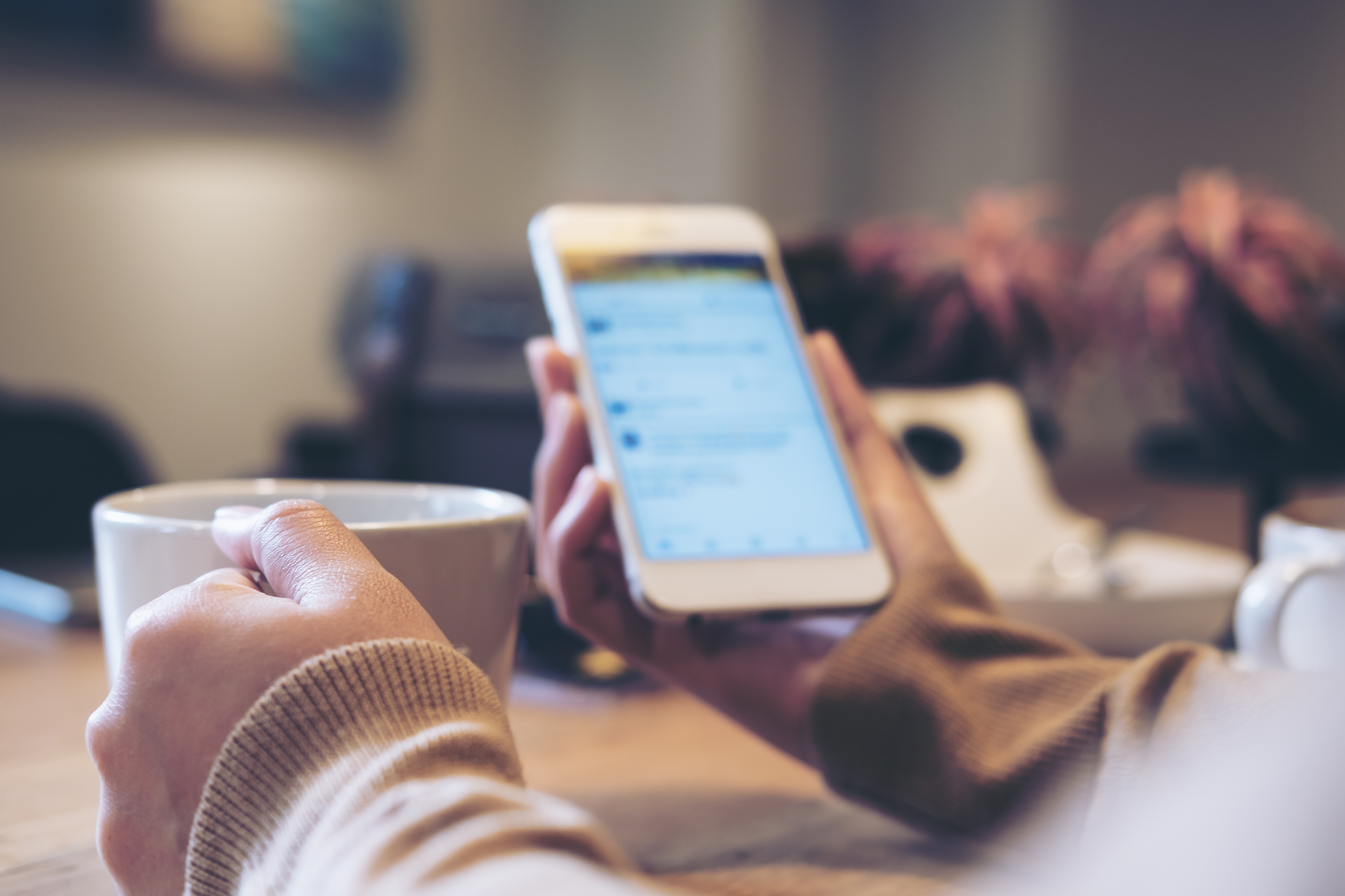 Person sitting at the table with hot drink and mobile phone in hand